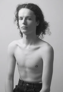 Portrait of a shirtless young male model with long curly hair against a neutral background for Numero Netherlands.