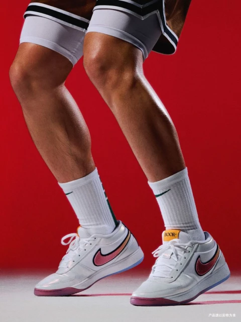 Close-up of a basketball player's lower body wearing white Nike shoes with a pink swoosh against a red background in a studio shot.