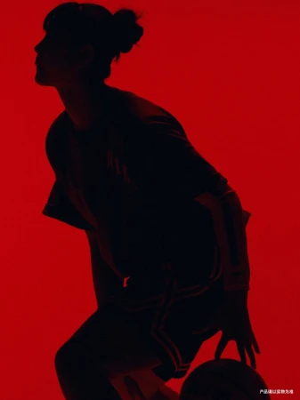 Silhouette of a woman in activewear dribbling a basketball against a vibrant red background with strong contrast and dramatic lighting.