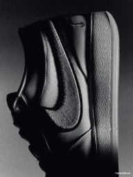 Close-up black and white product shot of a Nike sneaker showing textured sole and side swoosh logo against a dark background