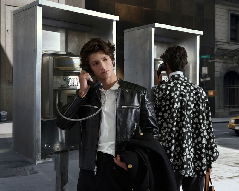 Two men standing near public phone booths on a city street. One man is on the phone, while the other is standing by a phone booth.