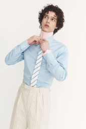 Young male model adjusting a striped tie wearing a light blue dress shirt against a plain white background