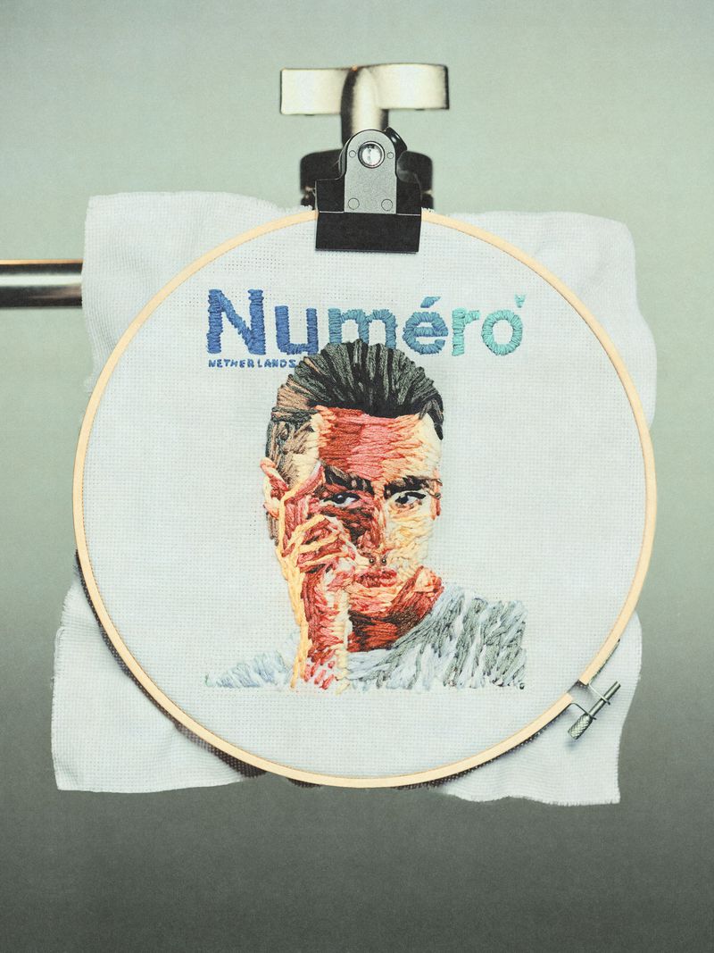 Embroidery art featuring a man's portrait and 'Numéro' logo, displayed on a towel rack, showcasing textile art and typography.