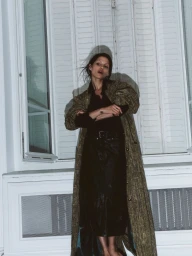 Model Gabbriette wearing a patterned coat against white shuttered windows