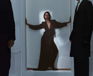 Model Gabbriette in a polka dot dress standing between two figures in dark suits for Pop Magazine