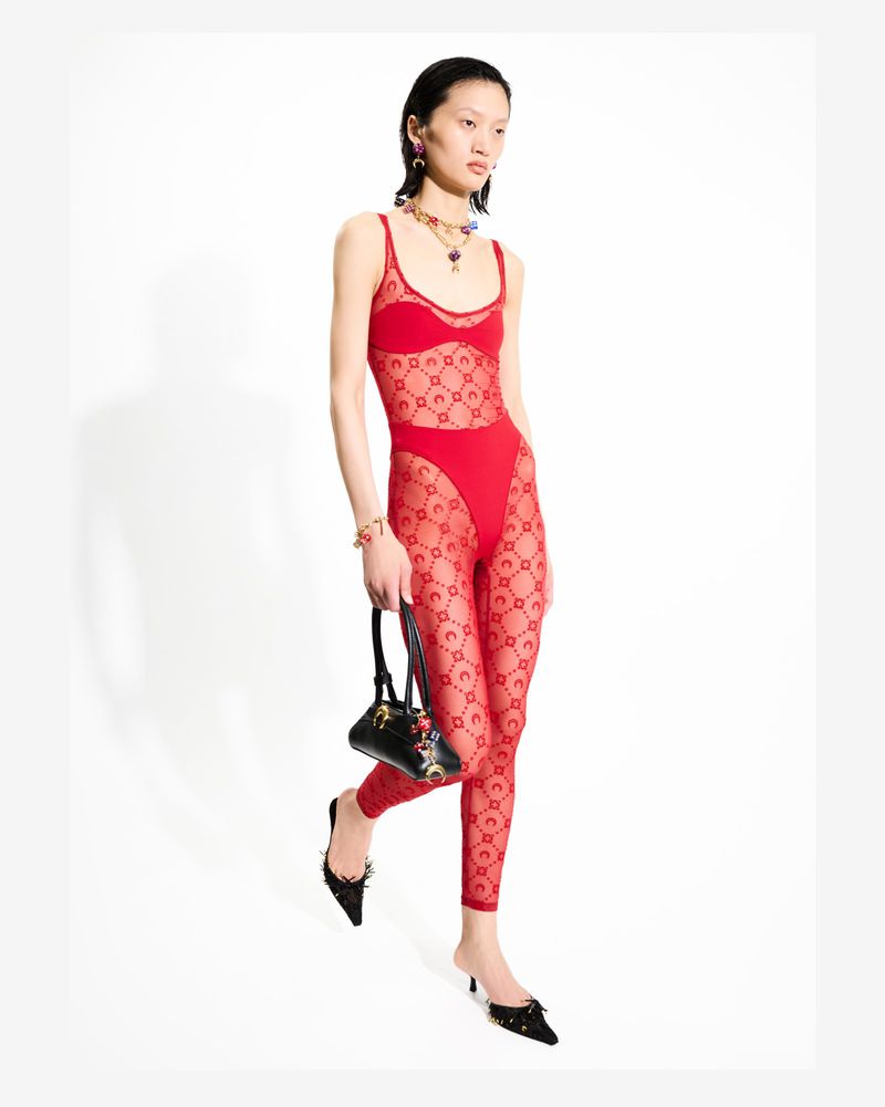A stylish Asian female model poses in a red patterned catsuit, holding a purse in a studio setting against a white backdrop.