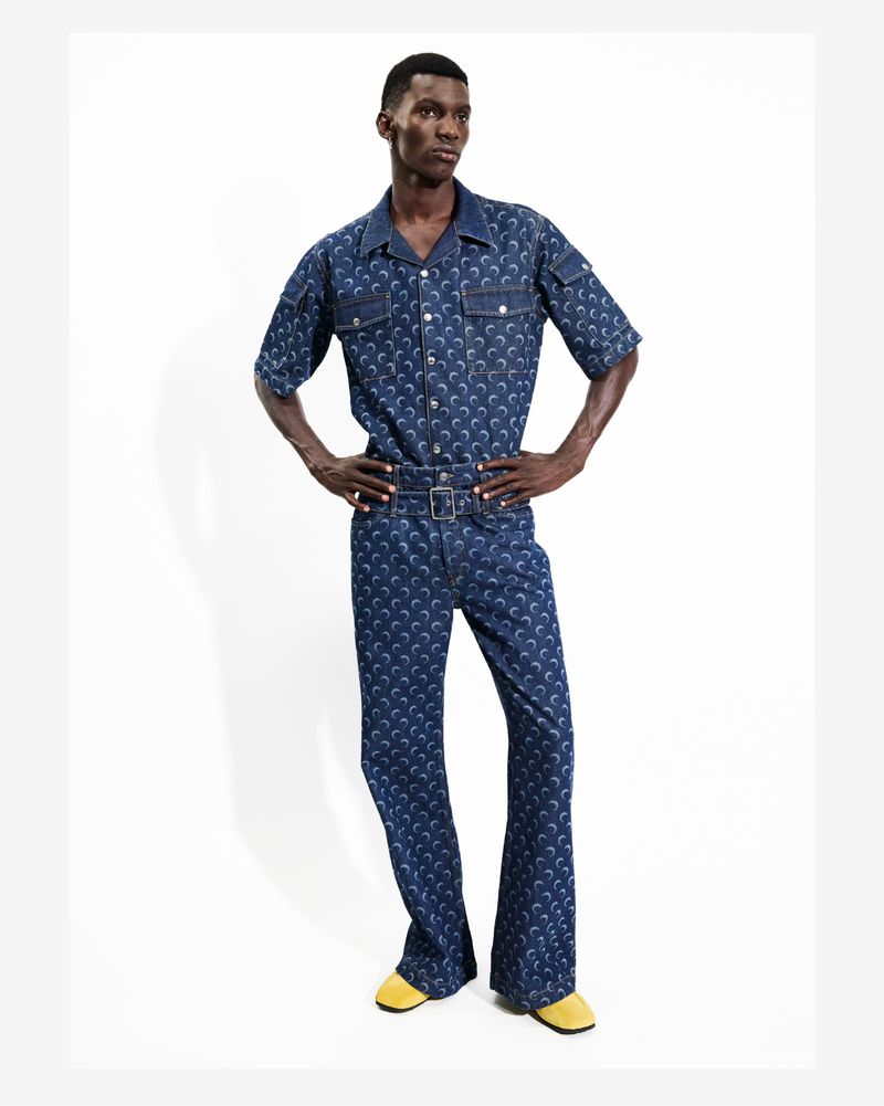 Fashion model poses in an all-over crescent moon print button-up shirt and wide-leg pants in a white studio, wearing mustard shoes.