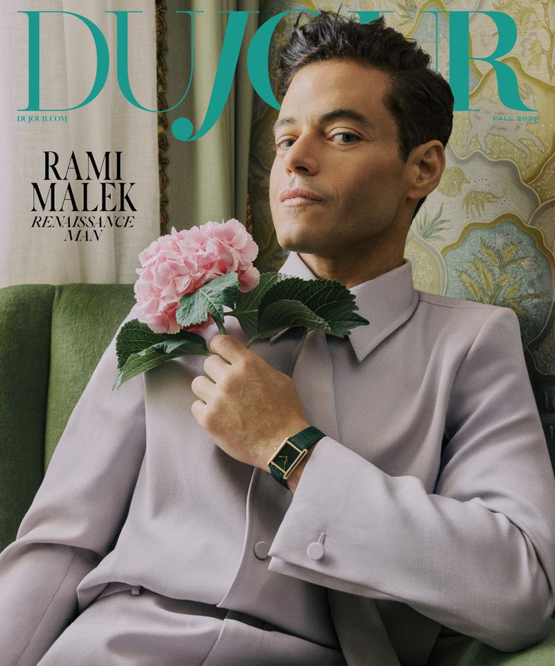 Rami Malek on the cover of DuJour magazine, wearing a lilac suit and holding pink hydrangeas, set against a patterned backdrop.