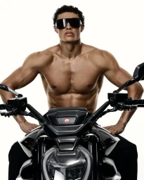 Shirtless male model wearing dark sunglasses seated on a black motorcycle against a white background