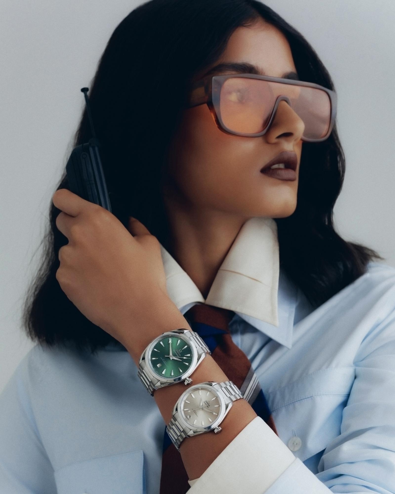 Woman with oversized glasses and a shirt wearing two silver wristwatches. Product photography of a watch with a green face and a silver face.