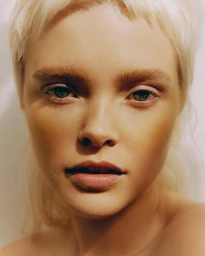 Close-up beauty portrait of a blonde woman with short hair and natural makeup against a plain background
