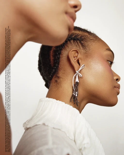 Close-up studio portrait of two Black women with braided hair, one wearing a silver bow earring, against a clean white backdrop.