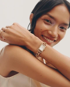 Smiling woman wearing a gold chain watch on her wrist against a neutral background for Net-A-Porter Fine Jewellery FW21
