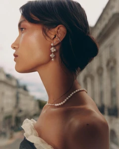 Profile portrait of a woman wearing pearl earrings and a pearl necklace outdoors with blurred buildings in background