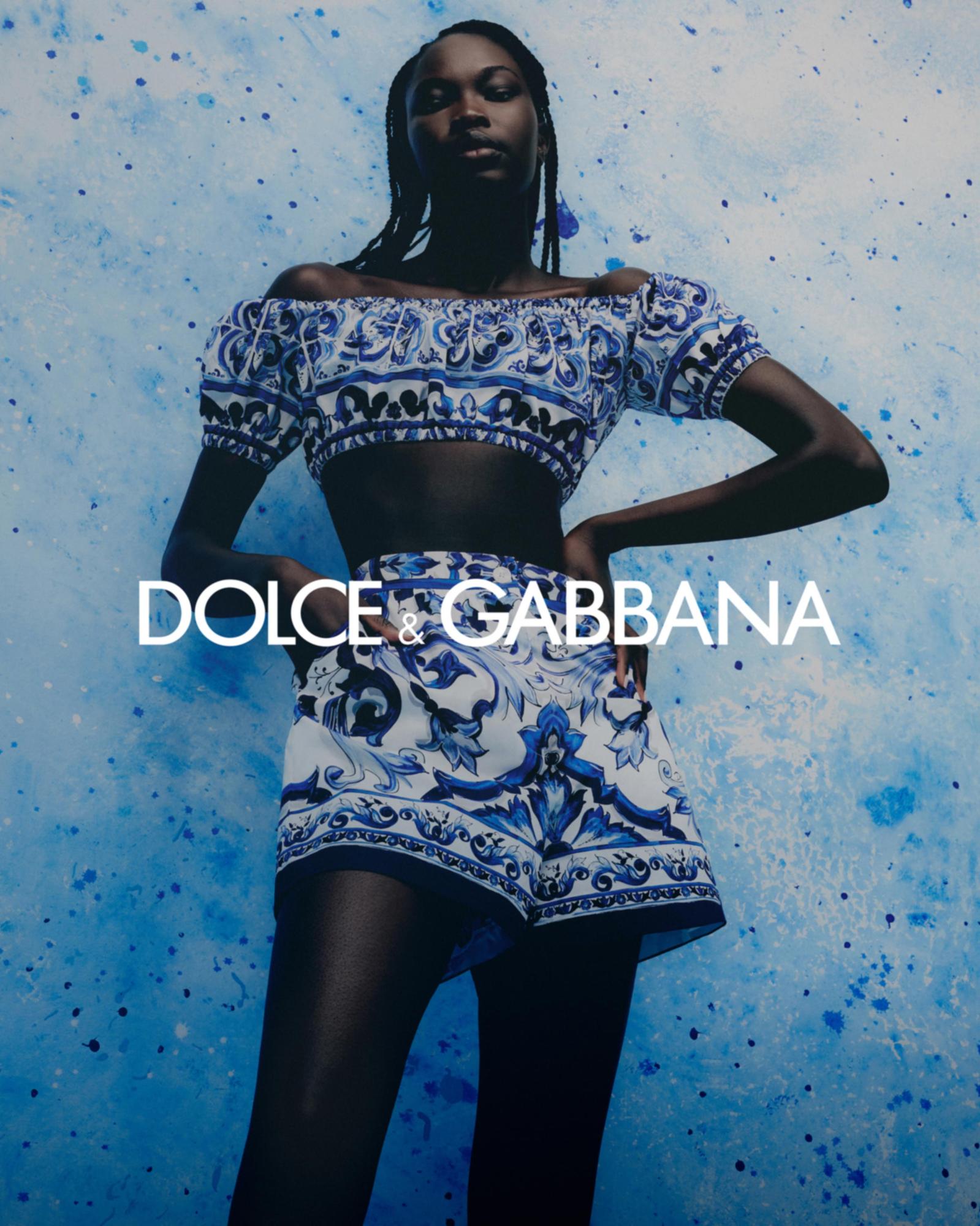 Fashion shot of a Black model wearing a blue and white patterned Dolce & Gabbana crop top and shorts against a blue background.