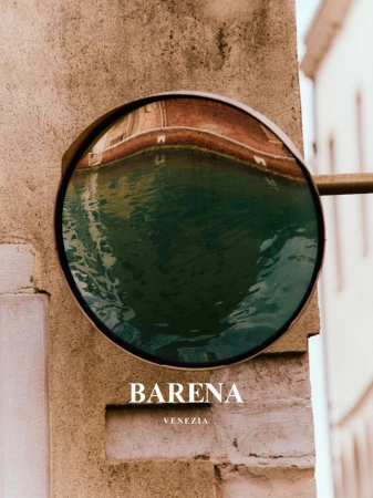 Architectural product shot of a canal reflection in a round mirror on a brick wall, featuring the BARENA VENEZIA logo below.