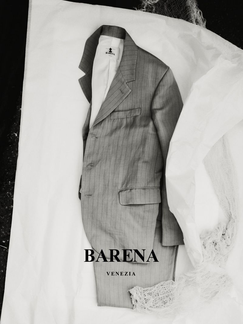 Studio shot of a pinstripe suit with a white shirt and logo on crumpled white paper, minimalist and monochrome.