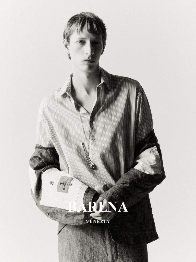 Editorial fashion shot of a blond male model in a striped shirt and jacket, posing against a white background, with the Barena Venezia logo.