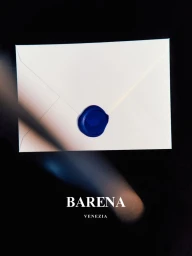 White envelope sealed with a blue wax stamp on a black background with Barena Venezia branding and a motion blur streak.