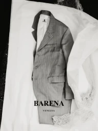 A tailored grey pinstripe suit laid flat on crinkled white paper with textured fabric draping along the right side.