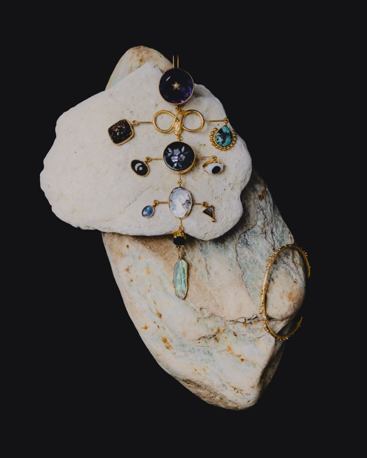Elevated product shot featuring a gold metal and gem statement pendant on a textured stone surface against a dark background. 
