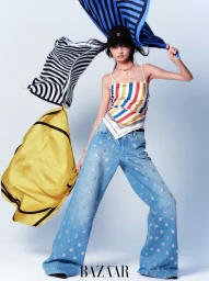 Model wearing patterned top and jeans with flowing scarves against a light grey background