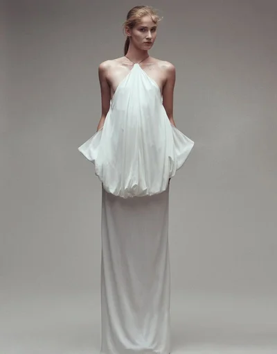 Model wearing a structured white halter dress standing against a neutral grey studio background for Vogue Adria
