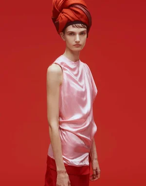 Model wearing a pink satin top and a large red turban against a red studio backdrop for Vogue Adria