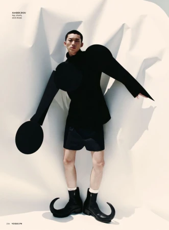 Editorial fashion shot of an Asian male model wearing a black jacket and shorts with sculptural paper art background and fantasy-style boots.