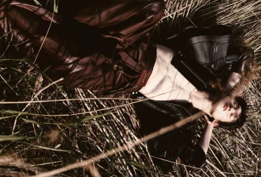 Model lying among tall dry grass wearing brown leather trousers and a black leather jacket for Vogue Man Philippines