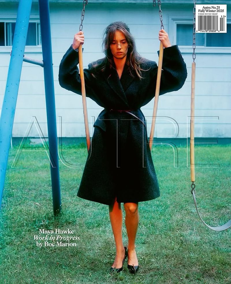 Maya Hawke posing on a swing wearing a dark coat in an outdoor setting, fashion editorial, medium shot.