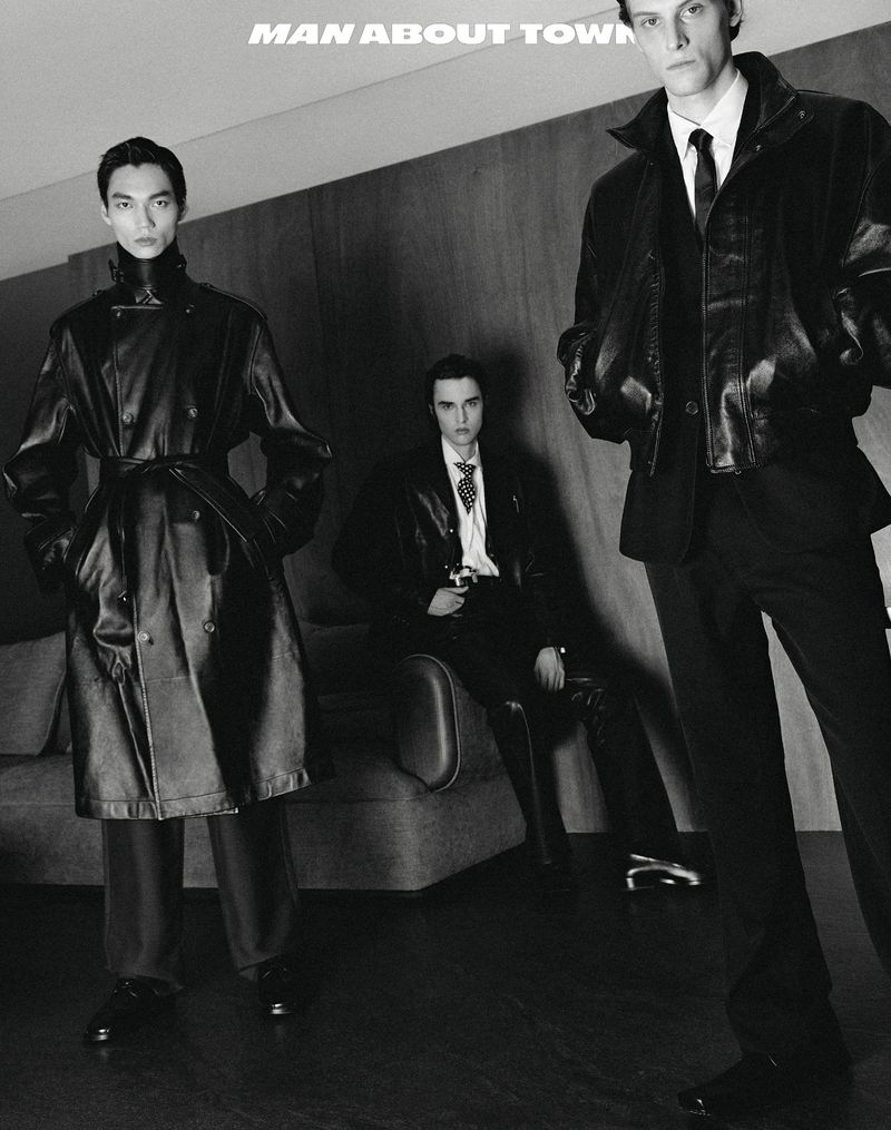 Three men in black leather jackets and suits pose indoors, showcasing modern, edgy fashion in a monochrome editorial style.