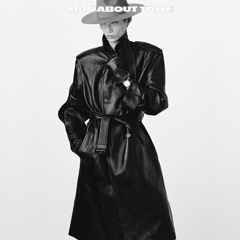 Monochrome portrait of an adult male in a hat and a long belted leather coat against a plain white backdrop.