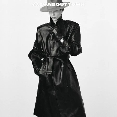 Monochrome portrait of an adult male in a hat and a long belted leather coat against a plain white backdrop.