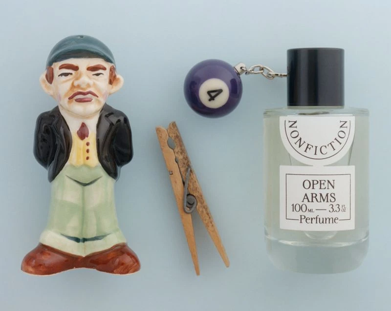 Still life photograph of a figurine, perfume bottle, pool ball, and clothespin arranged against a solid light blue background.