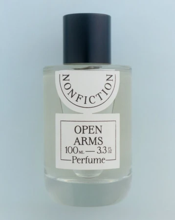 Clear glass bottle of Nonfiction Open Arms perfume with a black cap on a light blue background, centered and minimalist.
