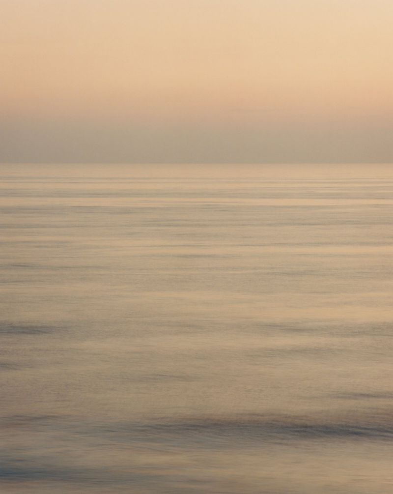 Horizon view of a calm ocean during golden hour, featuring a gradient sky and tranquil water surface.