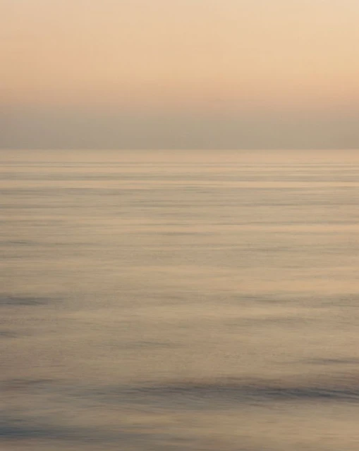 Horizon view of a calm ocean during golden hour, featuring a gradient sky and tranquil water surface.