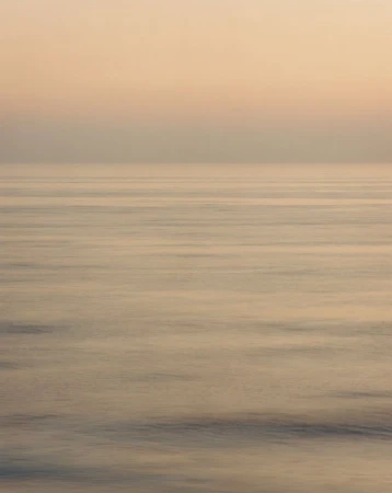 Horizon view of a calm ocean during golden hour, featuring a gradient sky and tranquil water surface.