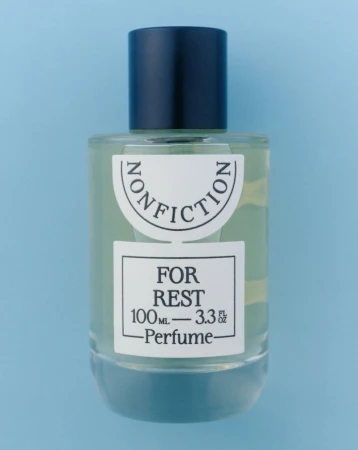 Studio shot of a Nonfiction For Rest perfume bottle with a black cap on a light blue background, showcasing its design and branding.