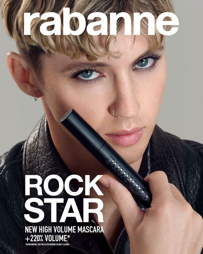 A person with short hair and a nose ring, wearing a leather jacket, holding a black mascara wand, with the brand name Rabanne above.