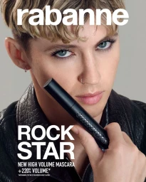 Troye Sivan holding a black mascara tube for Rabanne Rock Star campaign, wearing a black leather jacket against a grey background.