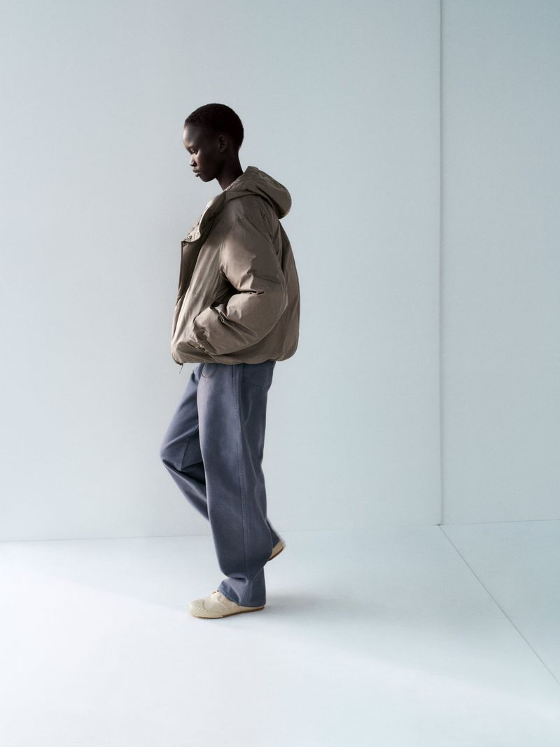 Fashion shot of an adult female wearing a puffer jacket, pants, and shoes in a photo studio with a white wall and floor.