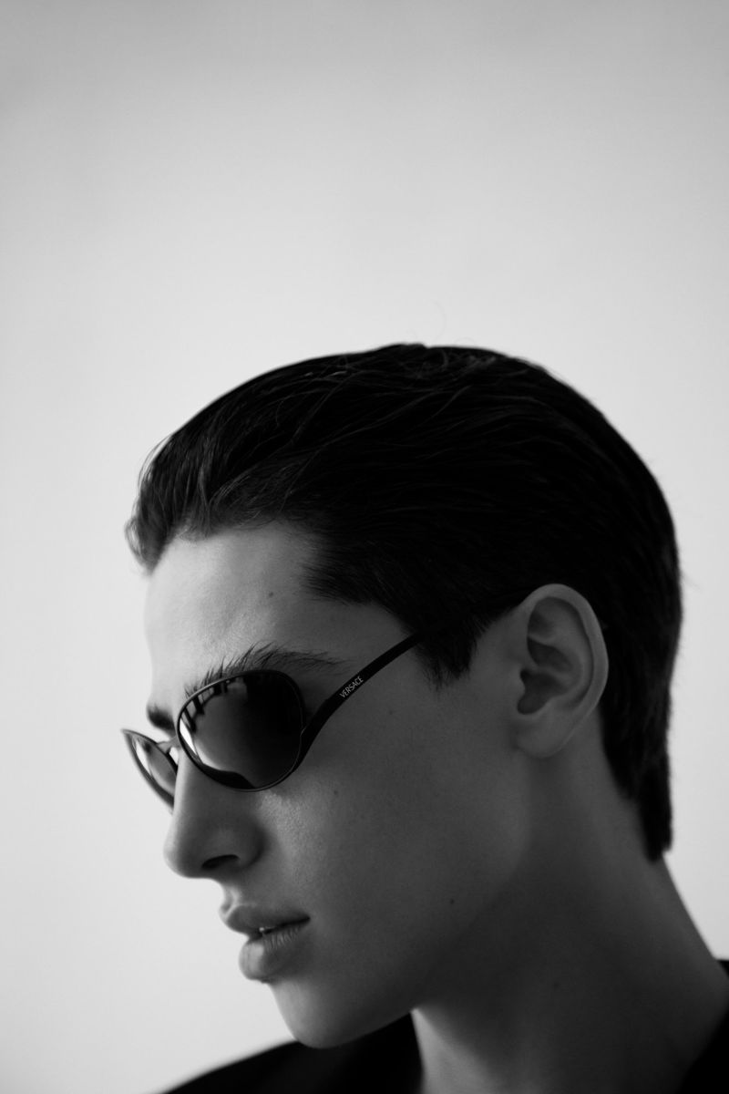 Monochrome portrait of a young adult with dark hair wearing sunglasses, showcasing a close-up view against a light background.