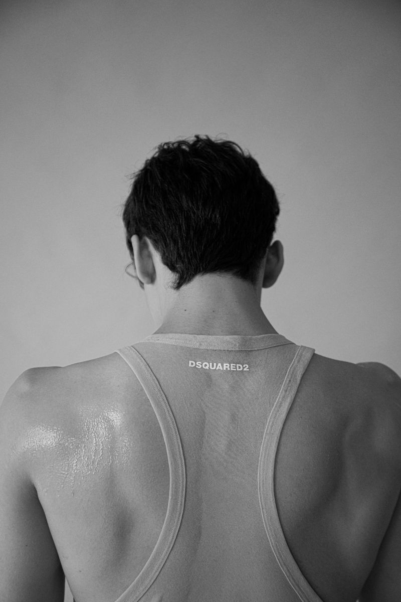 Black and white shot from behind of an adult male wearing a tank top, with visible back and shoulder muscles against a plain background.