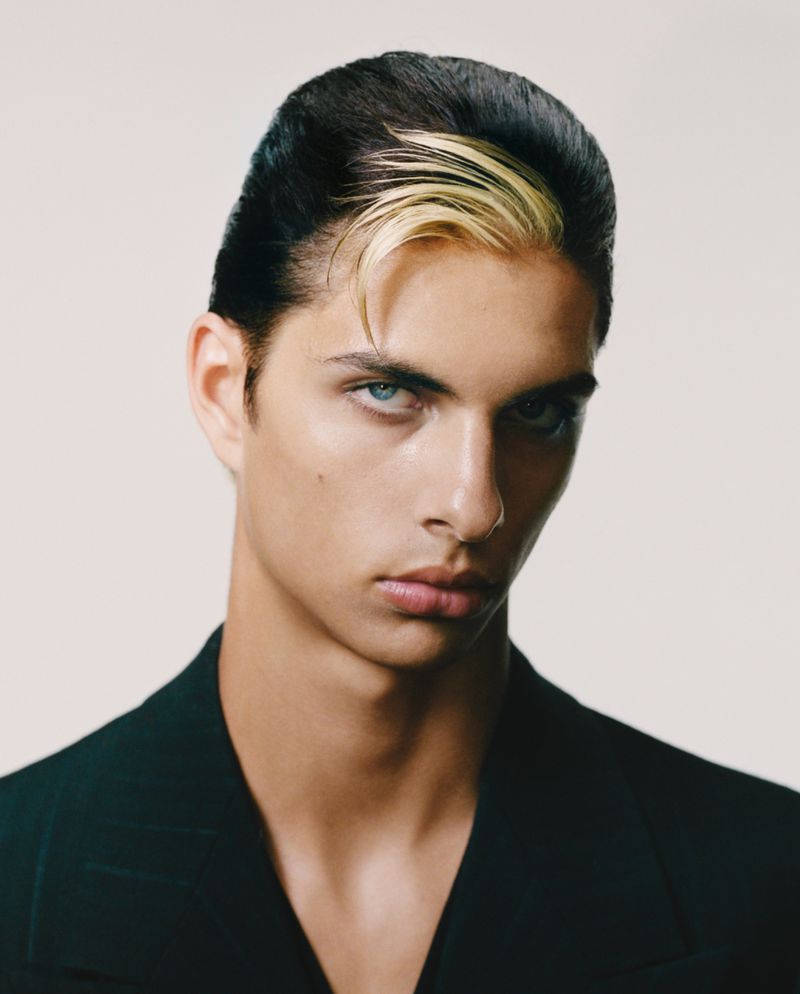 Headshot of a dark-haired male model with light blue eyes wearing a dark blazer. The lighting is neutral, and the background is off-white.