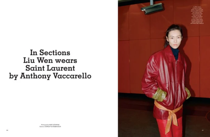 Editorial fashion portrait of a woman wearing a red leather jacket and pants, standing indoors against a red wall with a security camera.