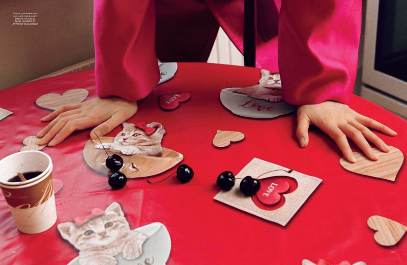 Overhead shot of a red table featuring playful cat-themed decorations, cherries, a coffee cup, and two women's hands.