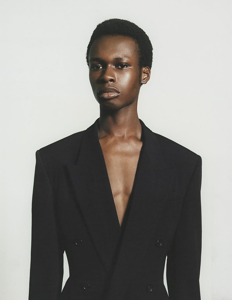 Elegant Black man in a dark blazer with an open neckline against a clean white backdrop in a head and shoulder portrait orientation.