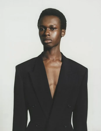 Elegant Black man in a dark blazer with an open neckline against a clean white backdrop in a head and shoulder portrait orientation.